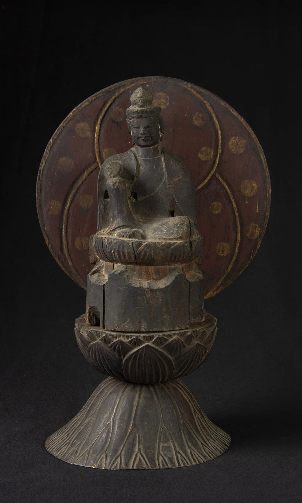 Carved wood folk bodhisattva seated in royal ease before a red and gold aureole on a lotus base, view 2 of 5