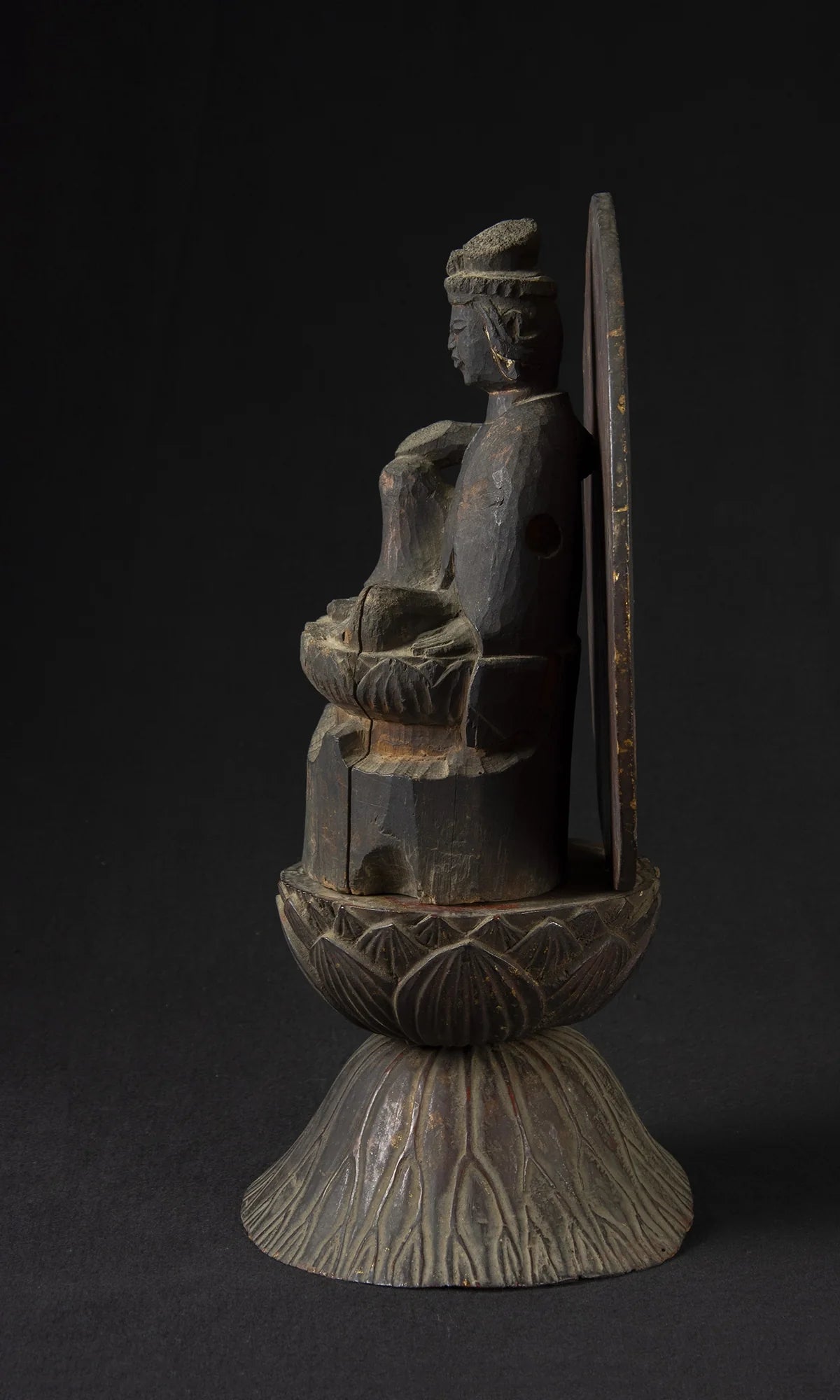 Carved wood folk bodhisattva seated in royal ease before a red and gold aureole on a lotus base, view 3 of 5