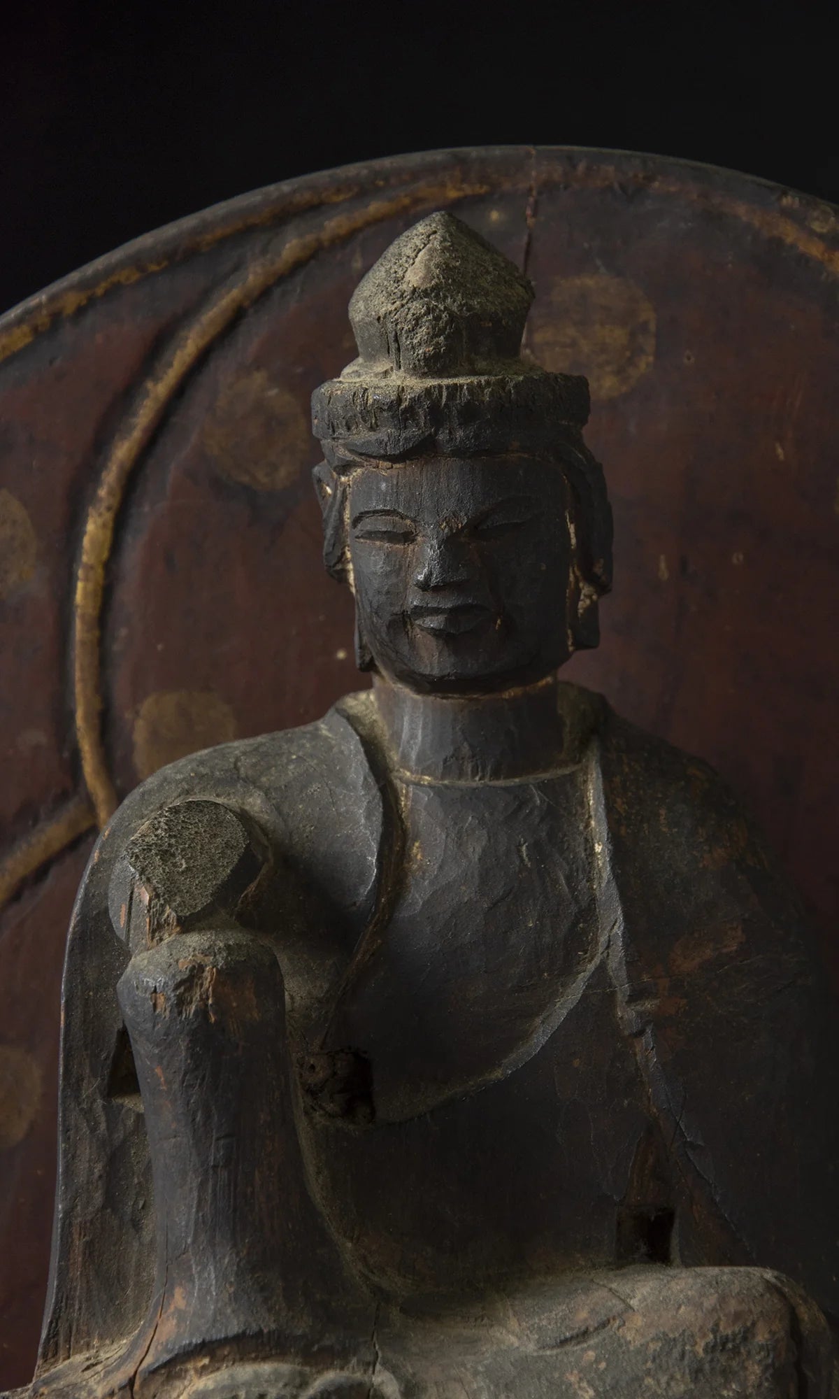 Carved wood folk bodhisattva seated in royal ease before a red and gold aureole on a lotus base, view 1 of 5